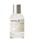 CR Signature Le Labo Santal 33 eau de parfum i en glassflaske med sølvkork mot en dramatisk sort bakgrunn med støv.